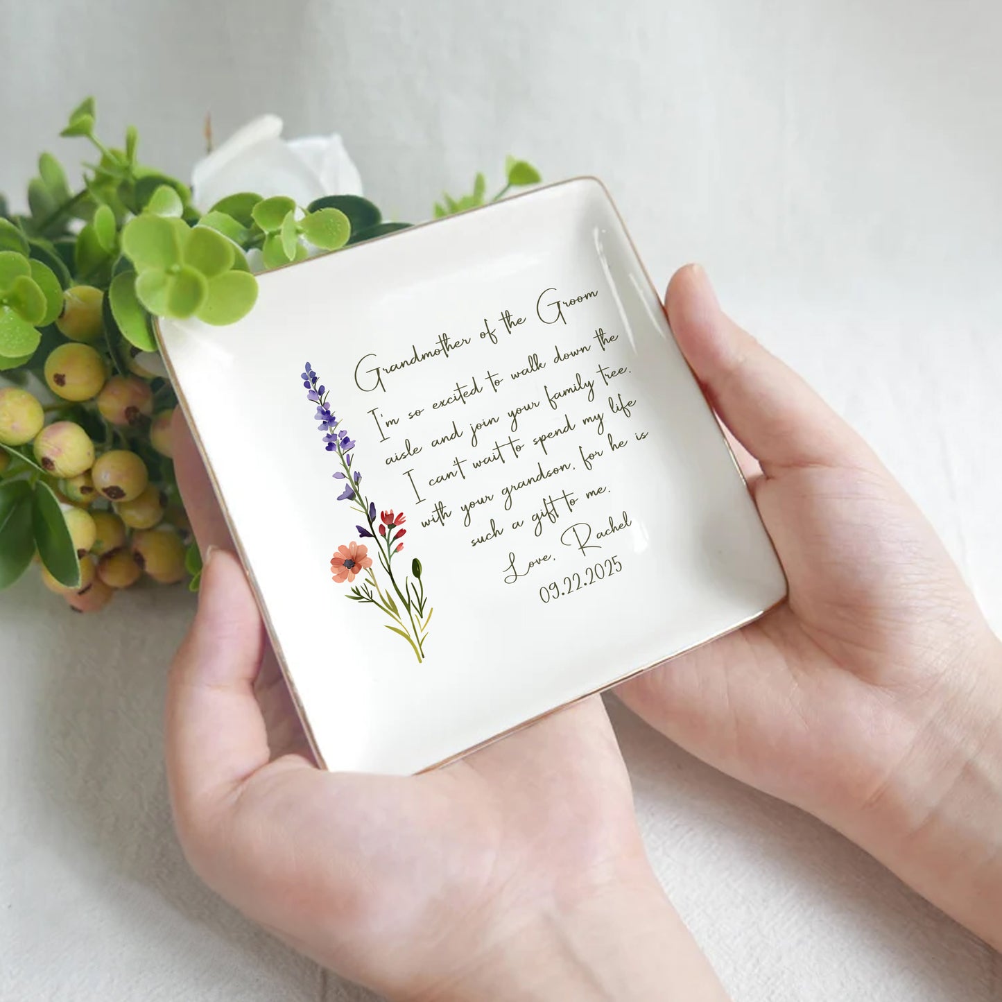 Person holding a decorative square plate with floral designs and text on a light background