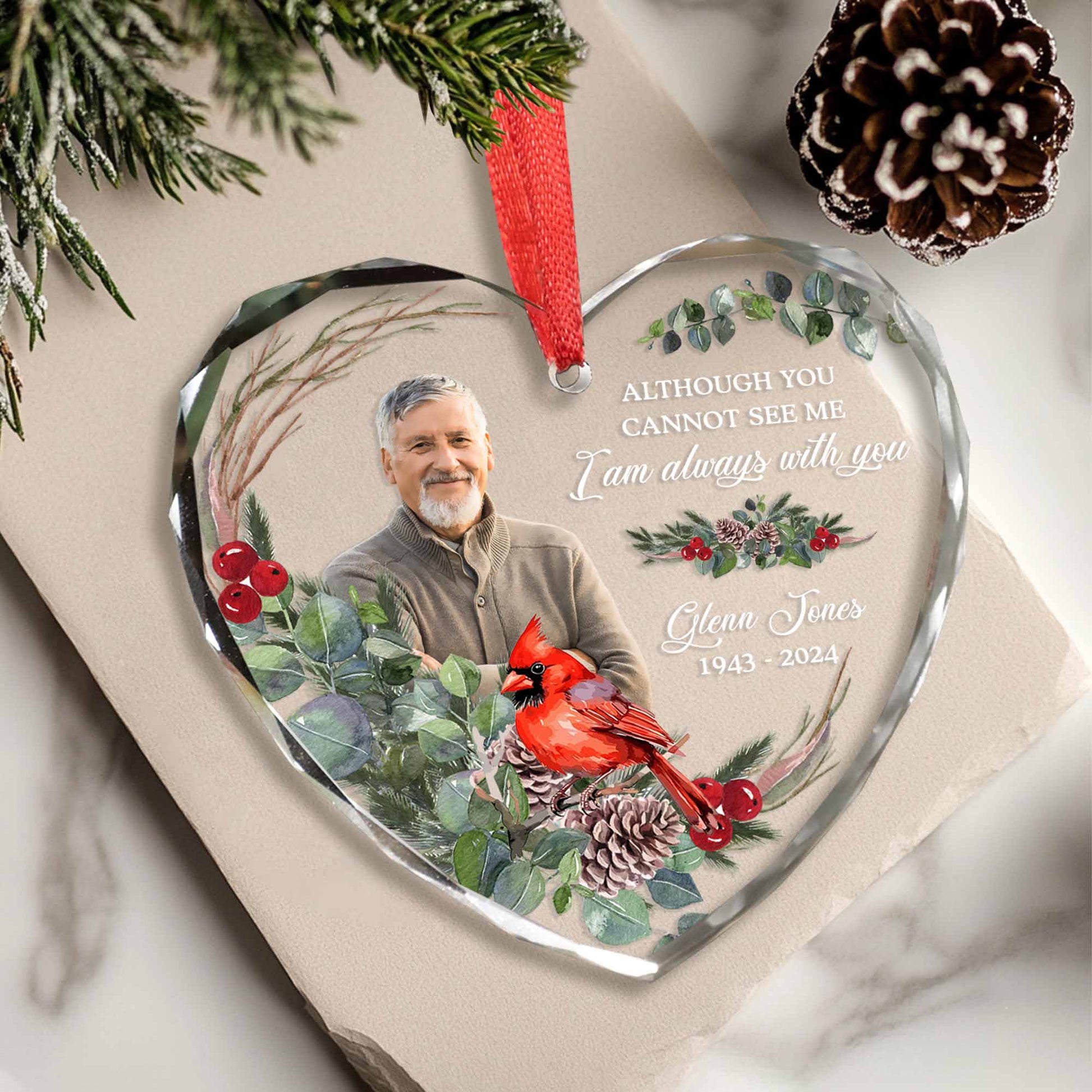 Heart-shaped glass ornament with a photo of a man, cardinal bird, and floral design on a marble surface.