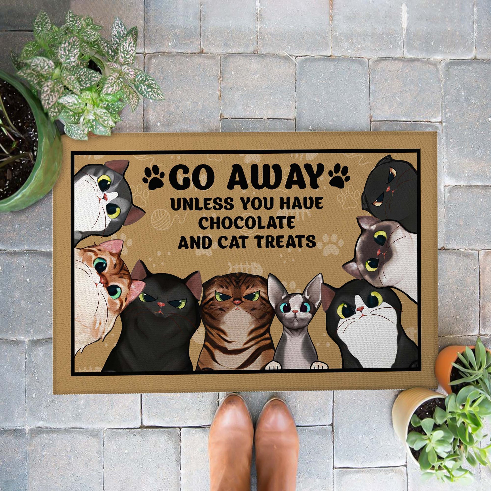 Doormat with cartoon cats and text 'Go Away Unless You Have Chocolate And Cat Treats' on a stone wall background.