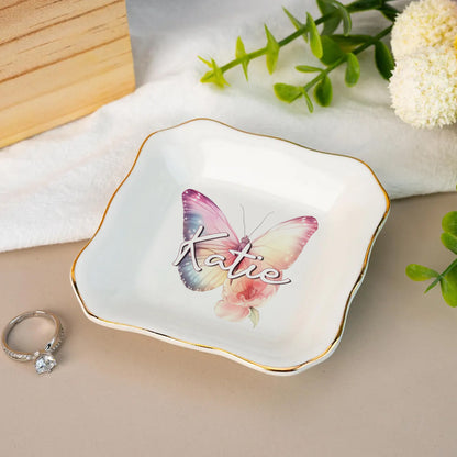 Personalized jewelry dish with butterfly design and 'Katie' text, placed on a surface with a ring and flowers.