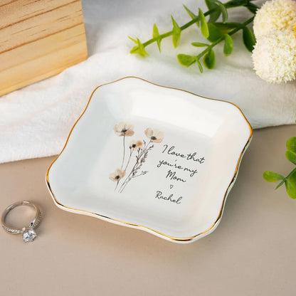 Decorative dish with floral design and text, placed on a surface with a ring and flowers.