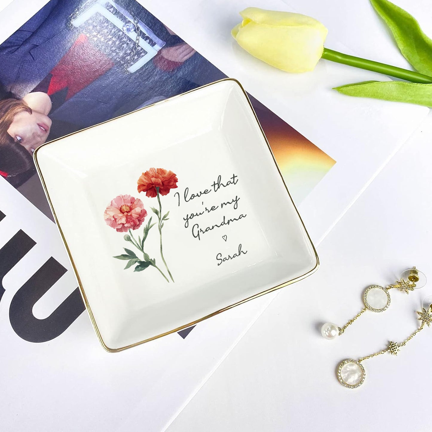 Decorative jewelry dish with floral design and text, placed on a magazine with tulips and earrings.