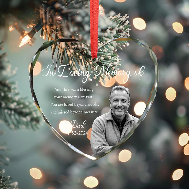 Heart-shaped glass ornament with a photo of a man and text 'In Loving Memory of' on a Christmas tree background.